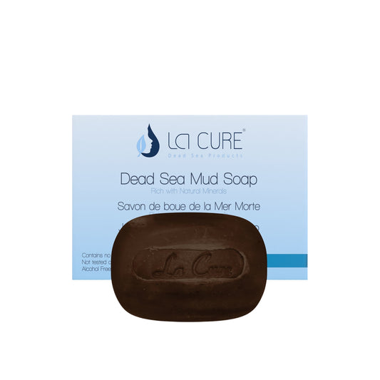 A bar of dark brown La Cure Dead Sea Mud Soap placed in front of its light blue and white packaging box on a plain white background.